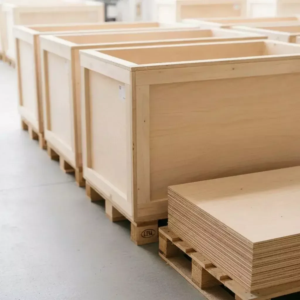 Open plywood export crates on pallets with a stack of plywood sheets