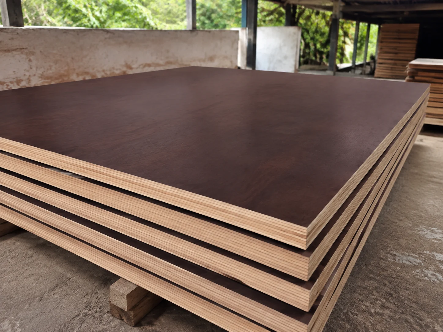 Brown film-faced shuttering sheets with layered edges in a shaded workshop